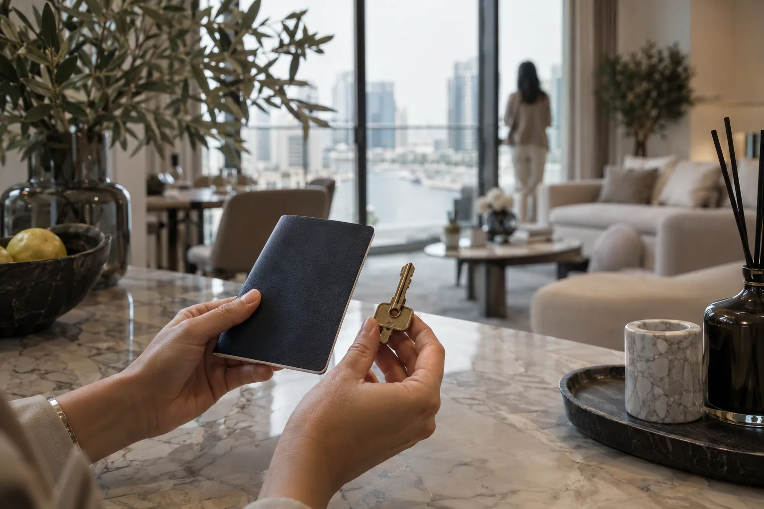 Hands holding a blank booklet and an apartment key on a marble countertop