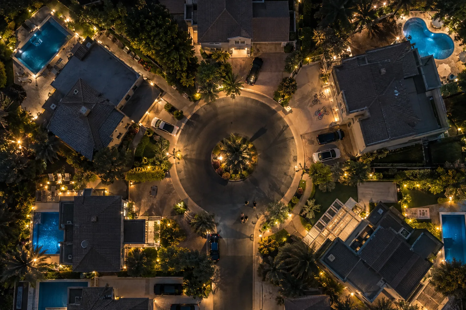 Nighttime aerial view of a cul-de-sac of lit villas with gardens and private pools