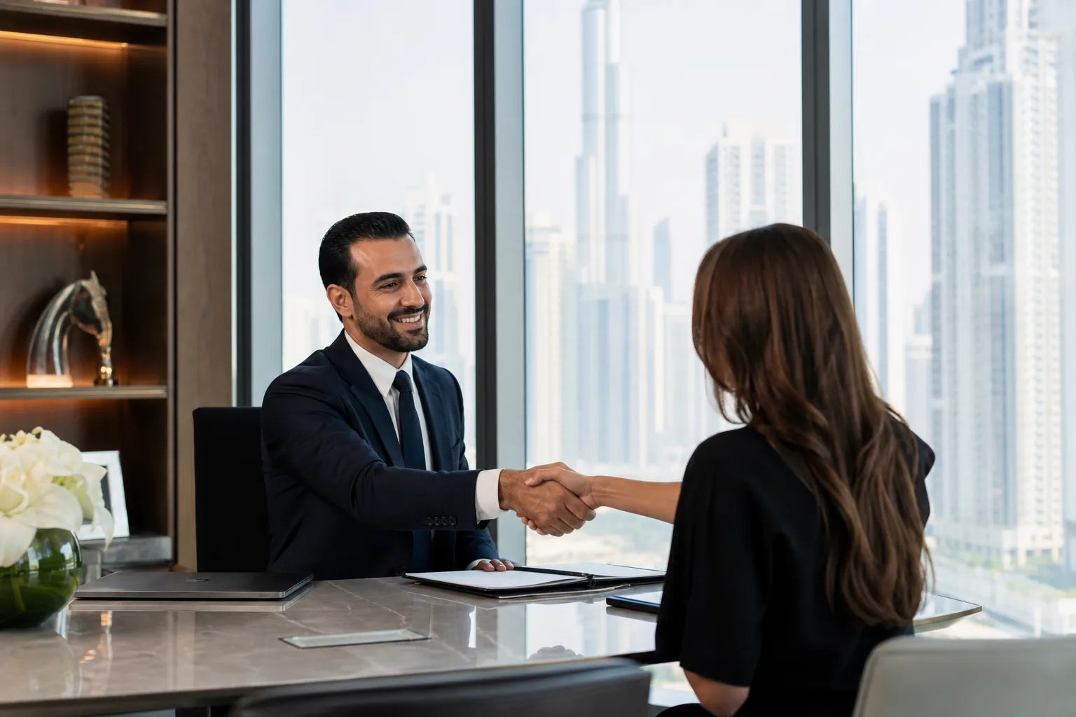 Handshake between an adviser and a client in an elegant office in front of the Dubai skyline
