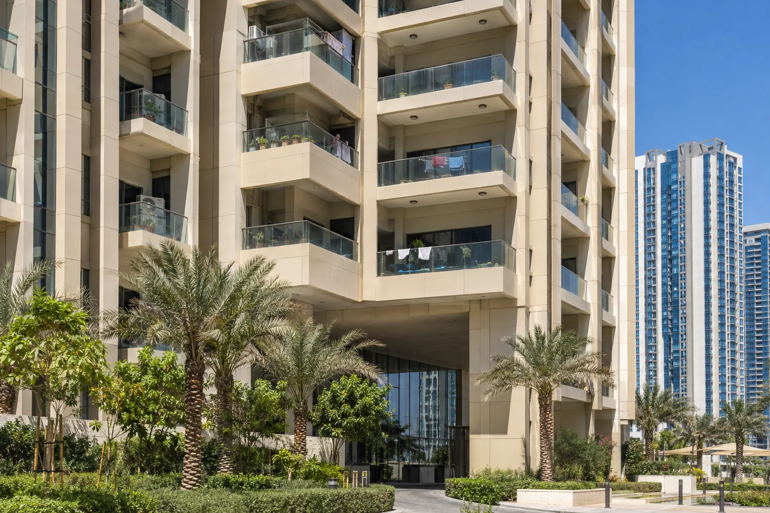 Facade detail of a Reem Island residential tower at midday, glazed balconies and palm trees at its base