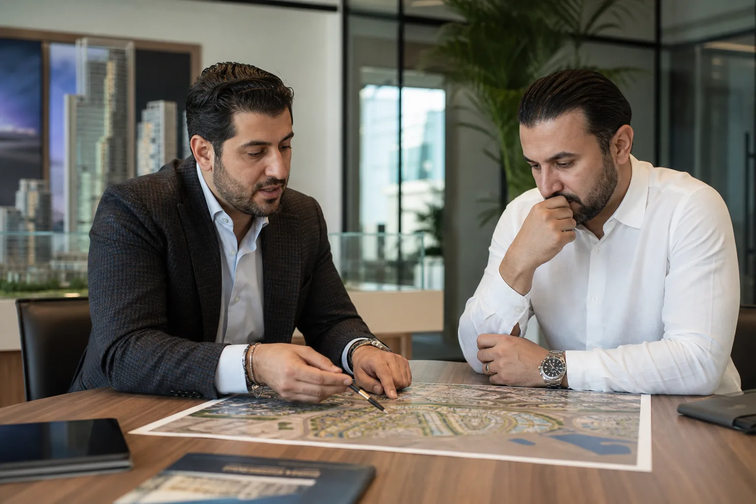 Conseiller pointant du doigt un plan de quartier tandis qu'un acheteur écoute attentivement dans une agence de Dubai