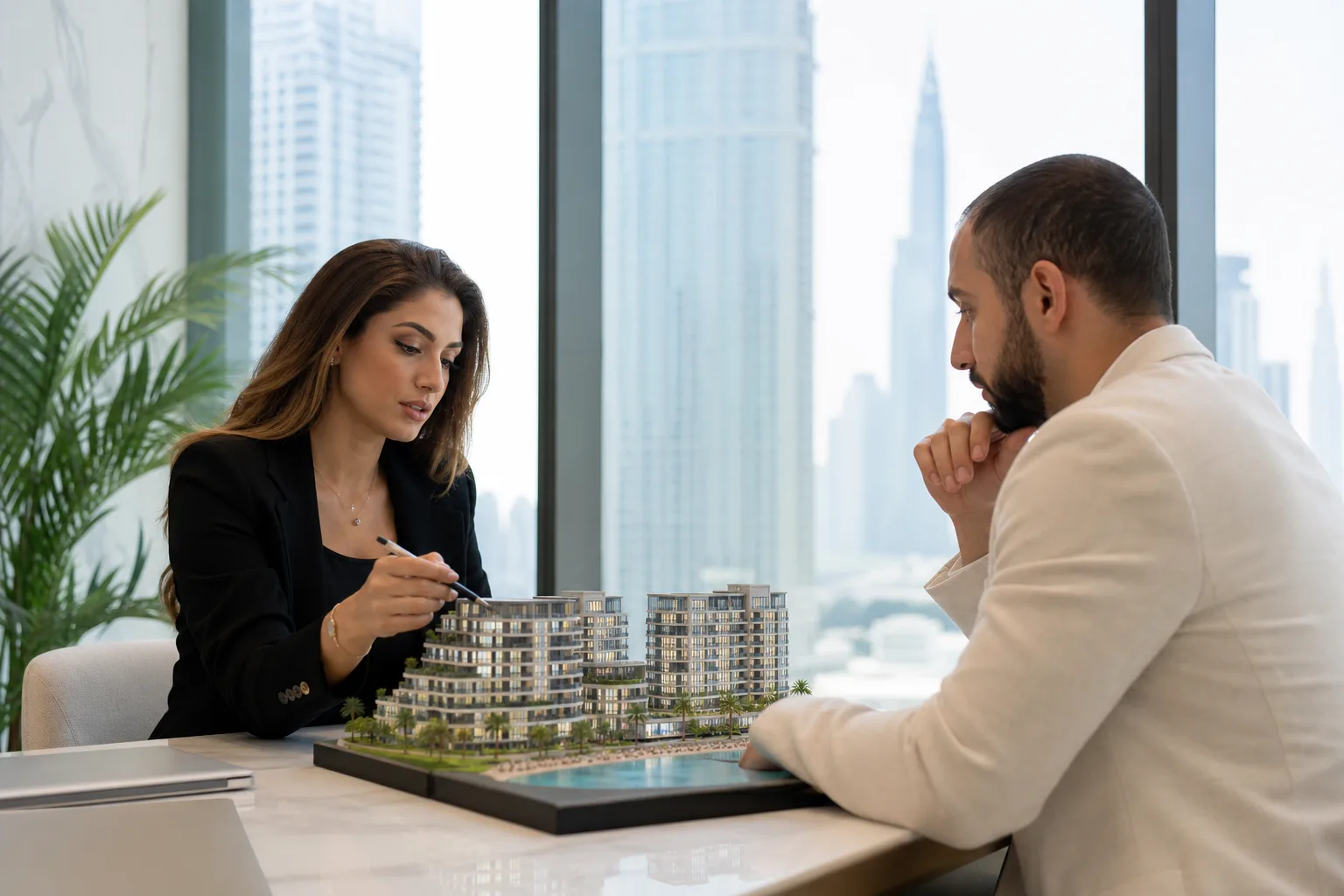 Client et conseiller assis à une table dans un bureau feutré de Dubaï examinant une maquette d'immeuble résidentiel