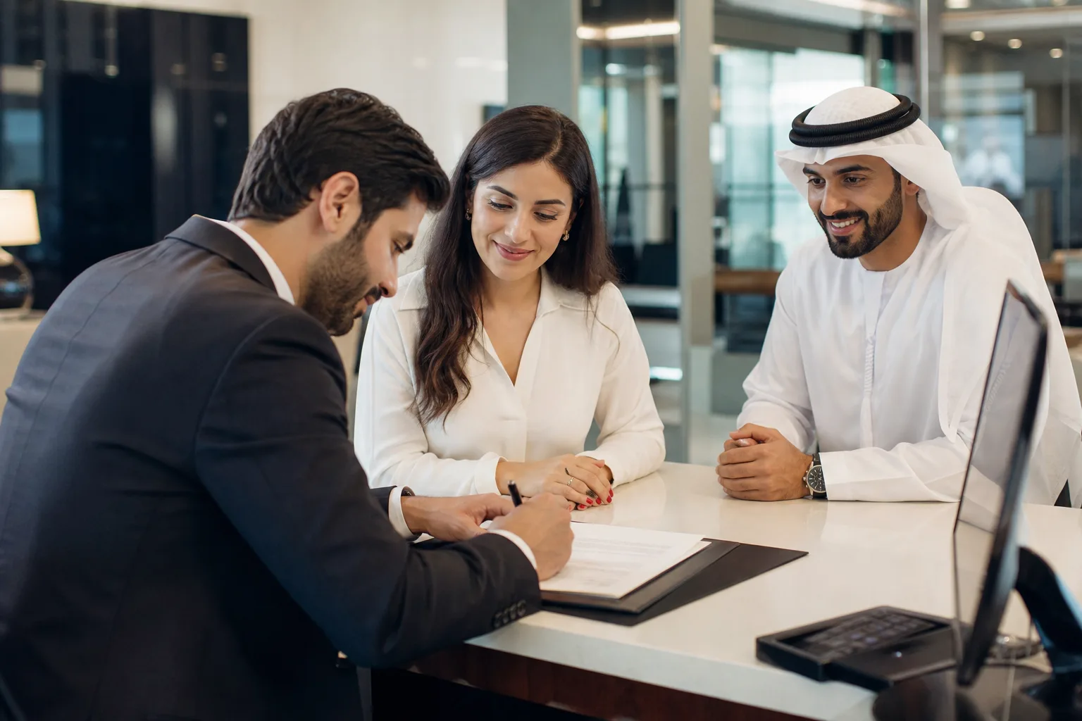 Client signant des documents au comptoir moderne d'une agence bancaire à Dubaï avec un conseiller souriant