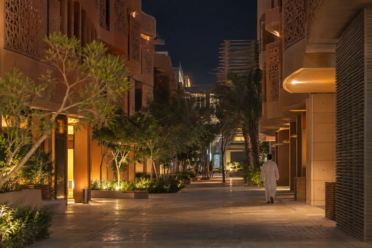 Pedestrian lane in Masdar City at night, low-rise buildings with perforated façades and a passer-by seen from behind