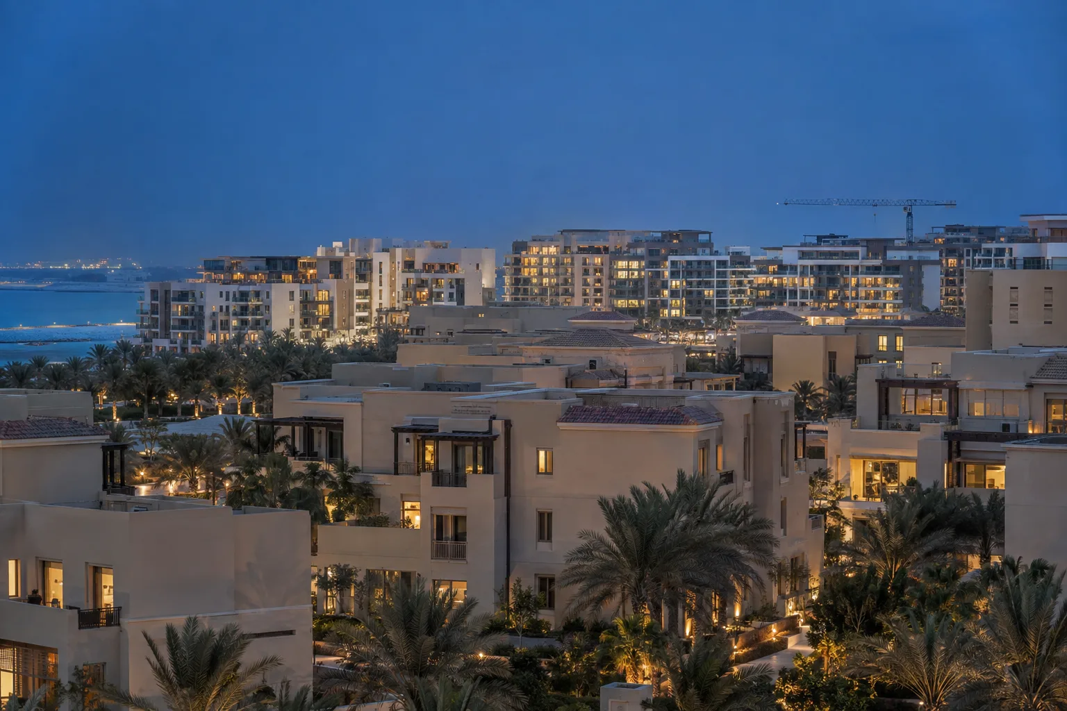 Saadiyat residences of different ages seen through a telephoto lens at blue hour, with a crane in the distance