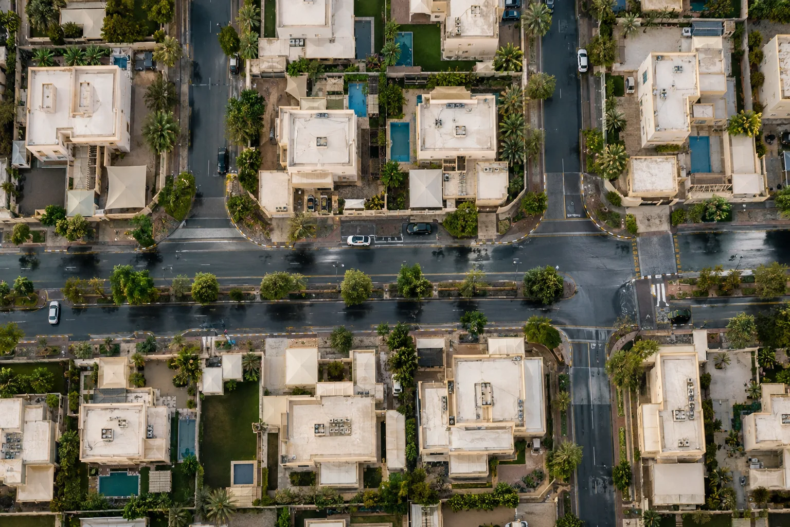 Overhead view of Al Bahyah villa streets after rain, with flat beige roofs and wet asphalt