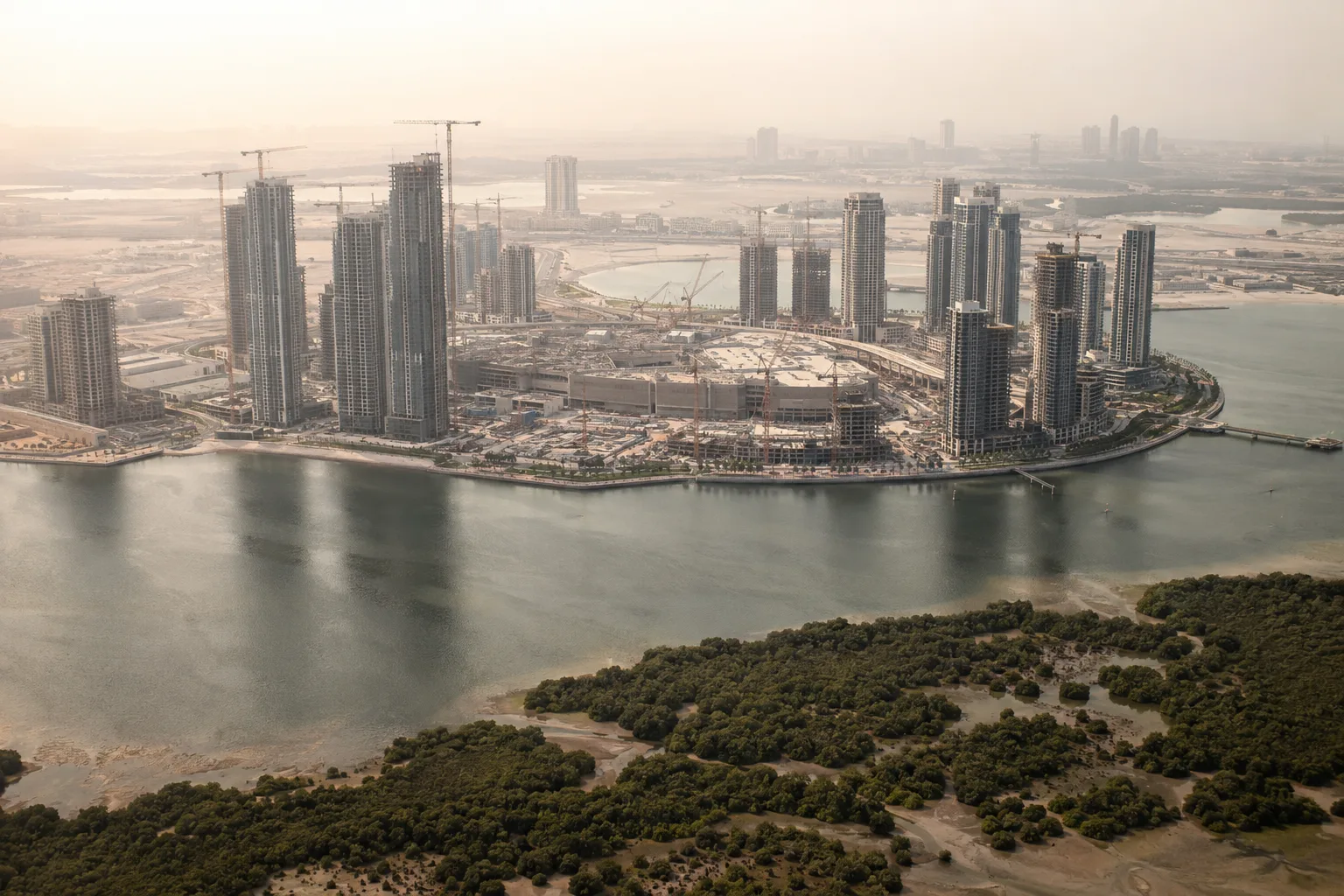 Oblique aerial view of Dubai Creek Harbour under construction, with cranes, residential towers and the creek in the foreground in a light haze