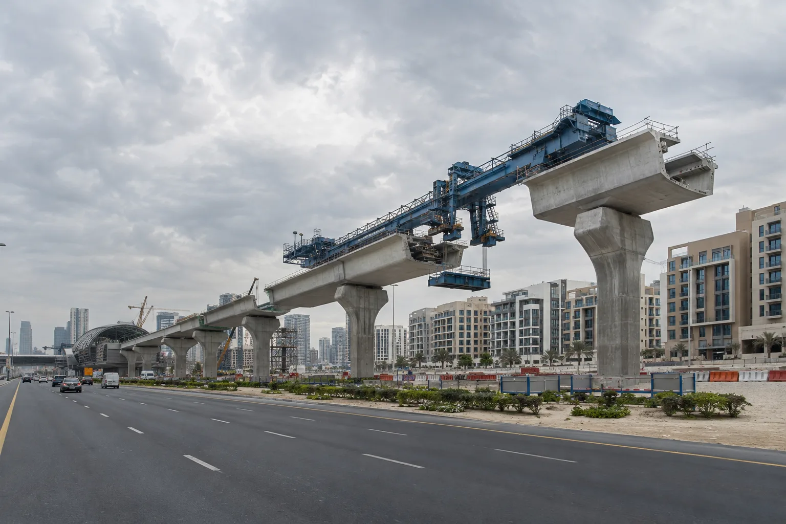 Elevated metro viaduct under construction in Dubai, running alongside a wide avenue and recent residential buildings