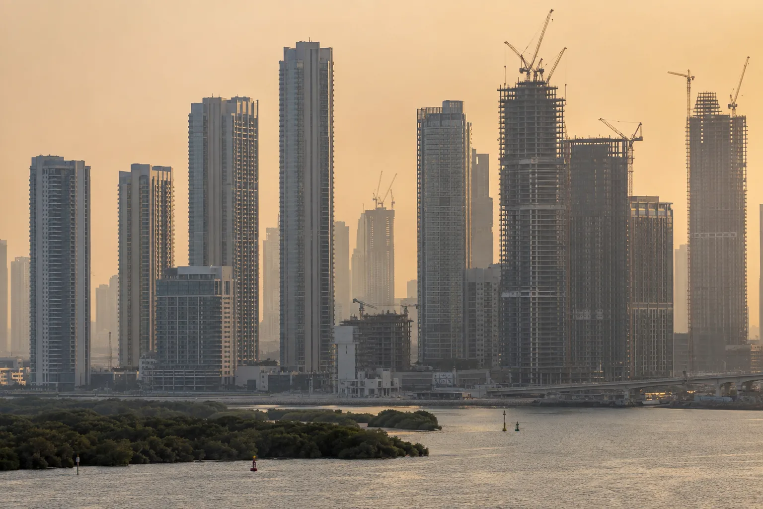 Residential towers of Dubai Creek Harbour seen through a telephoto lens from the opposite bank, in a dust haze
