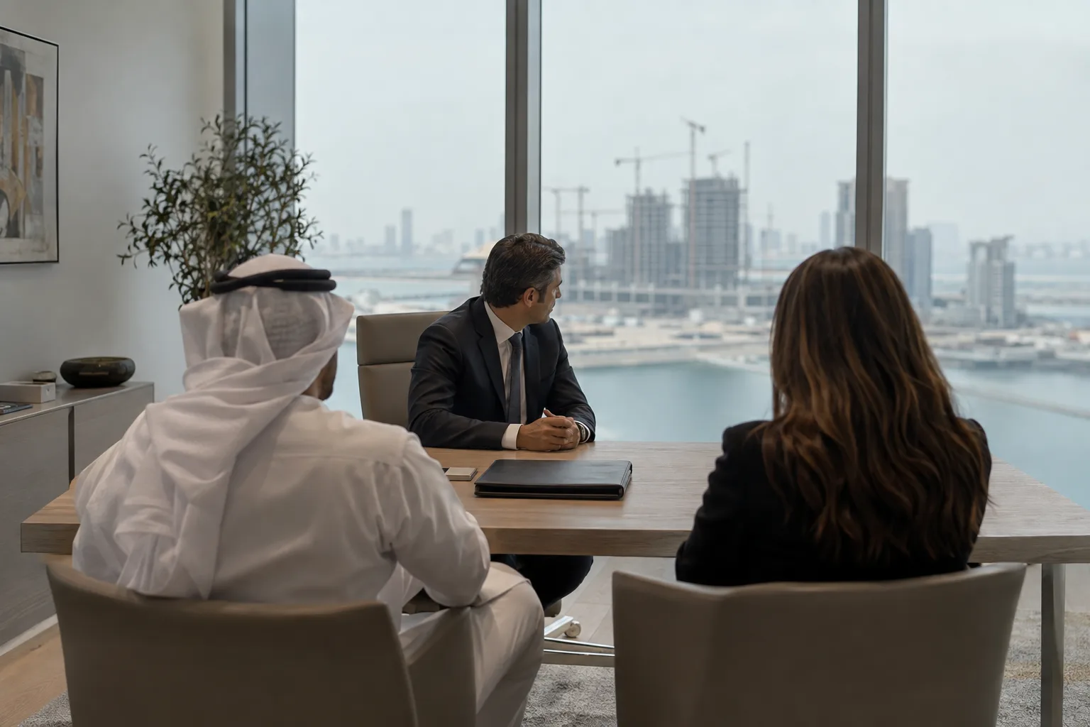 Two clients seen from behind facing an adviser at a table, a closed file between them