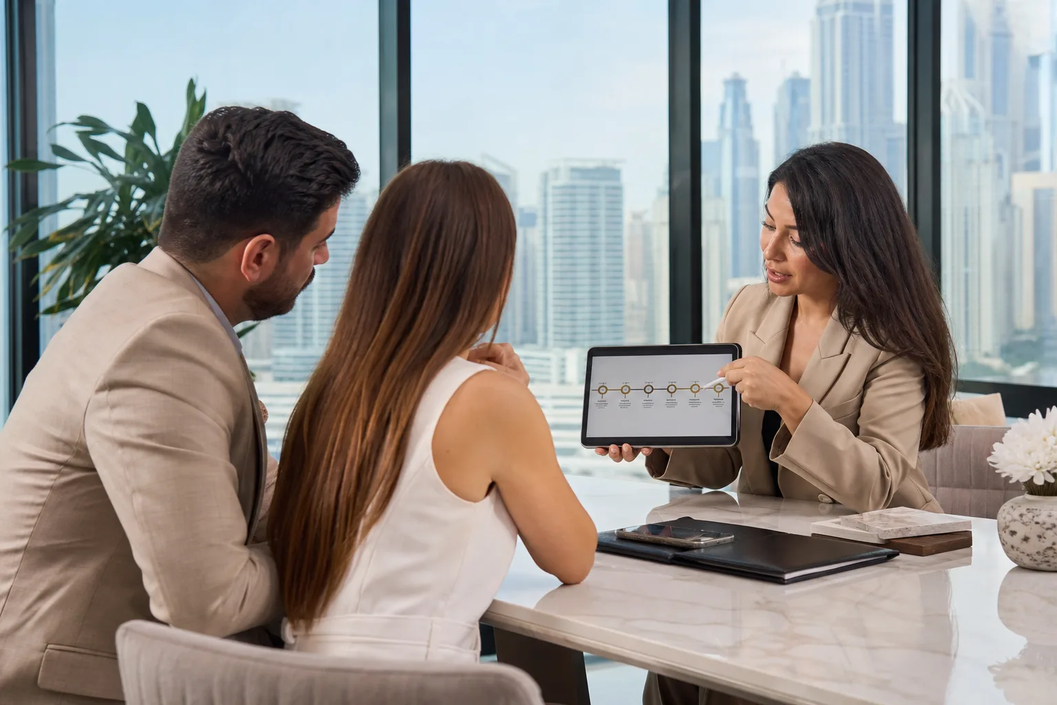 Conseiller immobilier présentant un échéancier sur tablette à des clients autour d'une table élégante