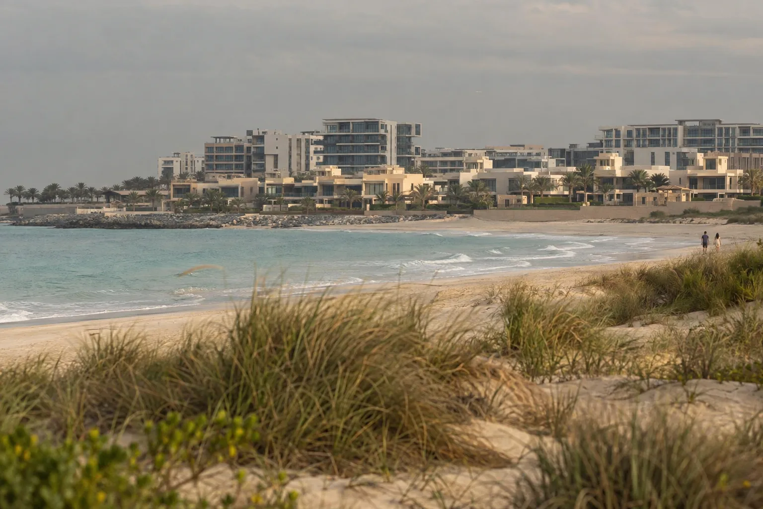 Saadiyat villas and low-rise buildings behind dunes and beach grass under a grey sky